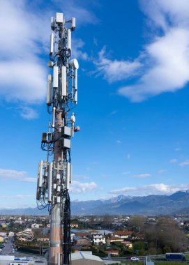 Cep telefonu sinyali yineleyici anten ve kablolar ile, metal bir direkte, mavi gökyüzüne ve bulutlara karşı. 