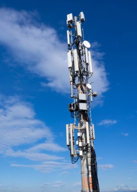 Cep telefonu sinyali yineleyici anten ve kablolar ile, metal bir direkte, mavi gökyüzüne ve bulutlara karşı. 