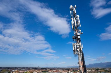 Cep telefonu sinyali yineleyici anten ve kablolar ile, metal bir direkte, mavi gökyüzüne ve bulutlara karşı. 