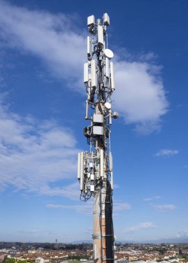 Cep telefonu sinyali yineleyici anten ve kablolar ile, metal bir direkte, mavi gökyüzüne ve bulutlara karşı. 