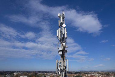 Cep telefonu sinyali yineleyici anten ve kablolar ile, metal bir direkte, mavi gökyüzüne ve bulutlara karşı. 