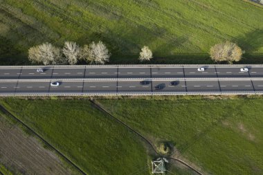 Yeşil kırsal kesimden geçen yoğun bir otoyolun hava manzarası, hareket halindeki arabalar ve yan taraflarında ağaçlarla. 