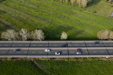 Yeşil kırsal kesimden geçen yoğun bir otoyolun hava manzarası, hareket halindeki arabalar ve yan taraflarında ağaçlarla. 