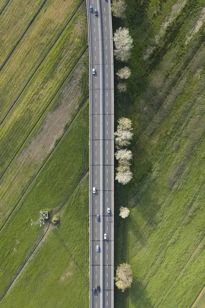 Yeşil kırsal kesimden geçen yoğun bir otoyolun hava manzarası, hareket halindeki arabalar ve yan taraflarında ağaçlarla. 