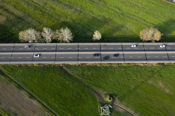 Yeşil kırsal kesimden geçen yoğun bir otoyolun hava manzarası, hareket halindeki arabalar ve yan taraflarında ağaçlarla. 