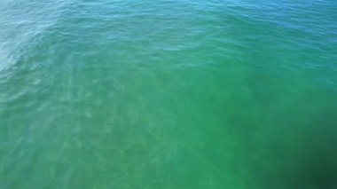 Güneş tarafından aydınlatılan ve yüzeyde yansıma ve ışık dalgalanmaları yaratan kumlu ve berrak bir deniz yatağının hava görüntüsü.. 