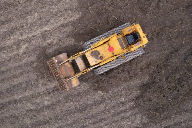 Yeni sürülmüş bir toprak tarlasında izleri olan sarı bir buldozerin detaylı hava fotoğrafları.. 