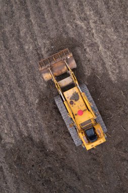 Yeni sürülmüş bir toprak tarlasında izleri olan sarı bir buldozerin detaylı hava fotoğrafları.. 