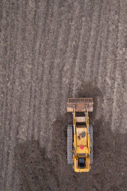 Yeni sürülmüş bir toprak tarlasında izleri olan sarı bir buldozerin detaylı hava fotoğrafları.. 