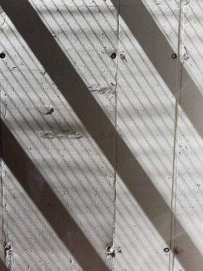 Keskin gölge çizgilerinin fotografik belgelendirmesi görülebilir dikey eklemleri olan açık gri betonun kaba bir yüzeyine çapraz olarak yansıtılır. 