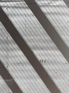 Keskin gölge çizgilerinin fotografik belgelendirmesi görülebilir dikey eklemleri olan açık gri betonun kaba bir yüzeyine çapraz olarak yansıtılır. 