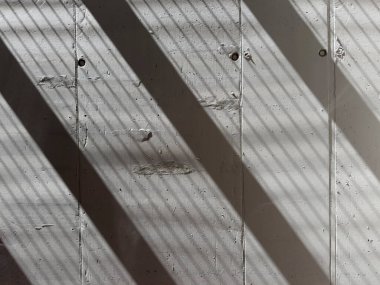 Keskin gölge çizgilerinin fotografik belgelendirmesi görülebilir dikey eklemleri olan açık gri betonun kaba bir yüzeyine çapraz olarak yansıtılır. 