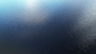 Sakin göl yüzeyinin hava görüntüsü dağınık bulutlu mavi gökyüzünü yansıtır.