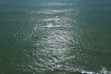 Dalgalanan denizin hava görüntüsü. Güneş ışığı yansımaları ve yumuşak dalgalar, rahatlatıcı ve doğal atmosfer..