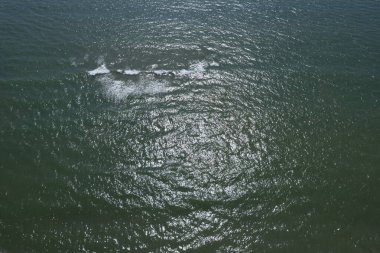 Dalgalanan denizin hava görüntüsü. Güneş ışığı yansımaları ve yumuşak dalgalar, rahatlatıcı ve doğal atmosfer..