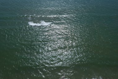Dalgalanan denizin hava görüntüsü. Güneş ışığı yansımaları ve yumuşak dalgalar, rahatlatıcı ve doğal atmosfer..