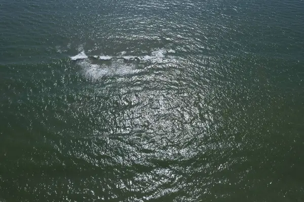 Dalgalanan denizin hava görüntüsü. Güneş ışığı yansımaları ve yumuşak dalgalar, rahatlatıcı ve doğal atmosfer..