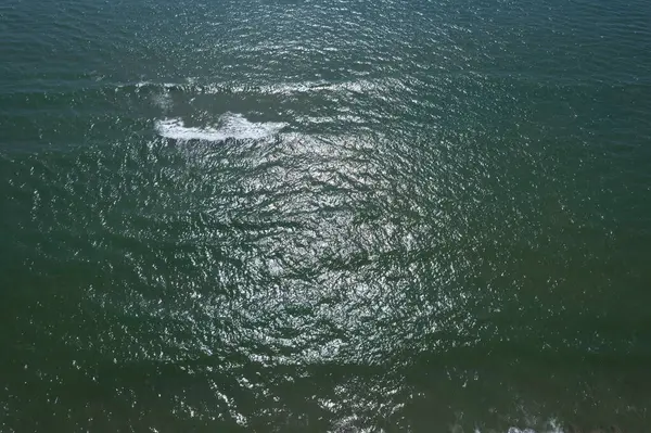 Dalgalanan denizin hava görüntüsü. Güneş ışığı yansımaları ve yumuşak dalgalar, rahatlatıcı ve doğal atmosfer..