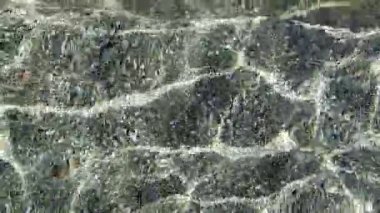 Dalgalanmalı bir su kütlesinin videosu eşsiz ışık oyunları yaratıyor, çakıl taşlarını ve deniz tabanındaki renkli yansımaları ortaya çıkarıyor.. 