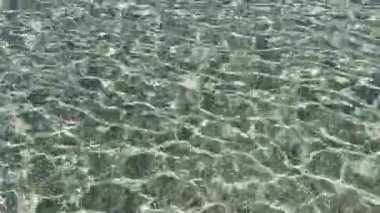 Dalgalanmalı bir su kütlesinin videosu eşsiz ışık oyunları yaratıyor, çakıl taşlarını ve deniz tabanındaki renkli yansımaları ortaya çıkarıyor.. 