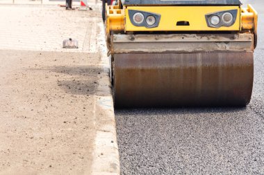 The wheel of a large road roller rams and compacts the new asphalt on the road lane. Close-up. Copy space.