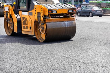A vibrating roller rams and compacts fresh asphalt on a city street on a summer day among the roadway. Close-up. Copy space.