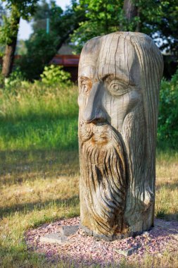Wooden carved statue of the head of a Ukrainian ancient peasant man on a blurred background of a green park. Vertical image. 06 19 2022. Kyiv. Ukraine.