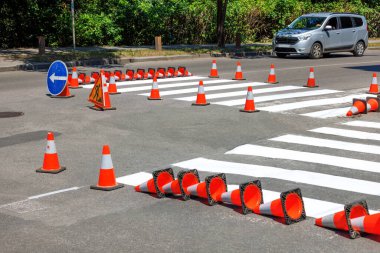 Application of pedestrian markings on the carriageway of a city road with a fence with orange traffic cones on a summer day.