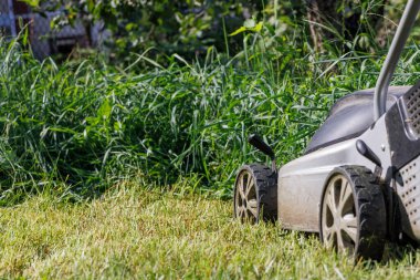 Mowing the lawn with an electric lawn mower. A fragment of the wheels of an electric lawn mower and green grass on a blurred background. Close-up. Copy space.