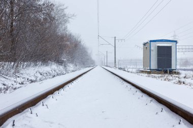 The railroad track and the transformer box were quickly covered with fluffy white snow during a snowfall on a winter day. Copy space.