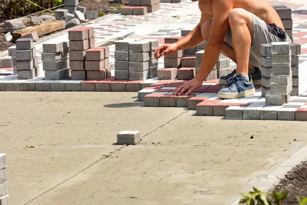 A worker makes a footpath by paving paving slabs, laying them on a sand base on a bright sunny day. Copy space.