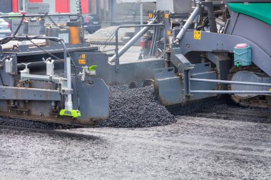 An industrial asphalt paver works on road works on a city road laying a fresh layer of asphalt.