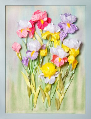 Cockerel flowers from the iris genus in a beautiful color composition and an art installation made of pieces of artificial fabric in a frame.