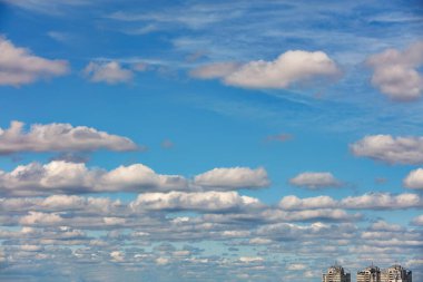 Ufuk çizgisine kadar uzanan bulutlarla dolu güzel mavi bir gökyüzü şehir evlerinin tepelerinden yükseliyor. Boşluğu kopyala.