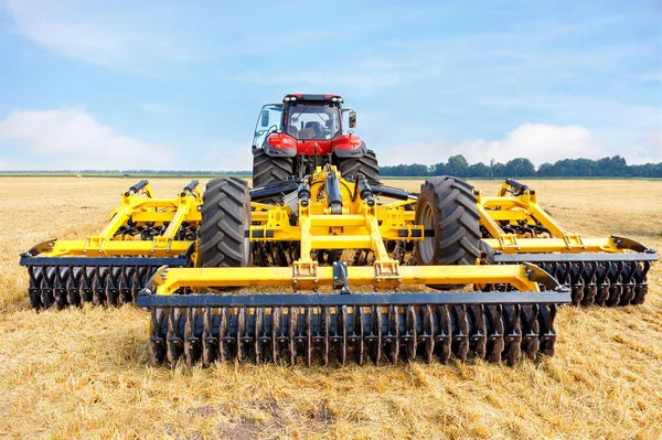 夏の収穫した小麦畑と青空を背景に 農業用トラクターに多列ディスクのハーローが取り付けられています — ストック写真