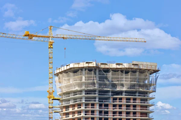 stock image Tower crane on the background of the construction of a multi-storey high-rise residential building against a blue cloudy sky. Copy space.