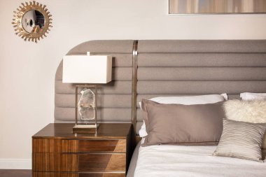 Yatak odasının içi pastel bej tonlarında yumuşak yastıklı, komodinli ve şık bir lambayla dolu..