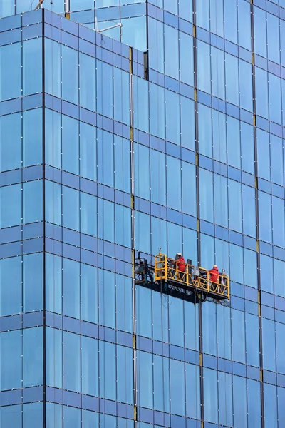 在现代住宅区 身穿红色工作服的建筑商使用悬挂式平台 对新房屋的正面进行釉面处理 边墙工程 复制空间 垂直图像 — 图库照片