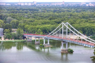 Kyiv 'deki Dinyeper Nehri' nin karşısındaki yaya köprüsünde ufukta yeşillik ve şehir binaları var..
