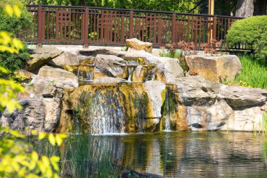 Kıyı şeridi boyunca taştan kayalarla çevrili bahçe göletine akan küçük bir şelale..
