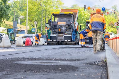 Yol inşaatçıları parlak ve sıcak bir günde yolda yeni asfalt döşeyip sıkıştırıyorlar. 05.20.23. Kyiv, Ukrayna.
