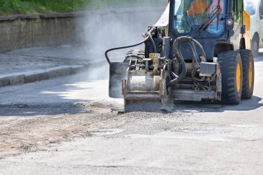 Üzerinde güçlü bir değirmen cihazı olan bir inşaat yolu traktörü leşin üzerindeki eski bir asfaltı kaldırır..