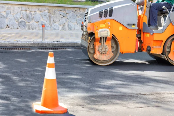 A construction roller lays fresh asphalt on the carriageway to resurface the road surface for cars.
