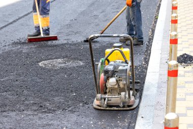 Yaya kaldırımının kaldırımındaki taze asfaltta duran yıpranmış bir vibratör tabağı asfaltı sıkıştırmak için çalışmayı bekliyor. kopyalama alanı. Boşluğu kopyala.