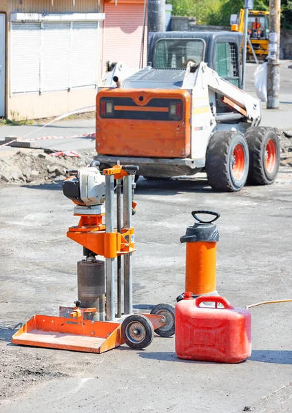 Drilling petrol machine to determine the thickness of the asphalt concrete pavement against the background of road machinery in blur on a clear day. Vertical image. Copy space.