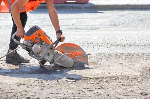 Bir işçi, güneşli bir yaz gününde, çalışma alanında, bir yol kenarının asfalt beton kaldırımını benzin kesici ile kesiyor. Boşluğu kopyala.