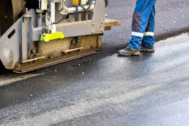 Asfalt beton fabrikasında endüstriyel asfalt kaldırım. Bir işçinin kontrolündeki asfalt kaldırımın bir parçası, bir şehir yolu inşa ediliyor, asfaltlama işlemi devam ediyor. Boşluğu kopyala.