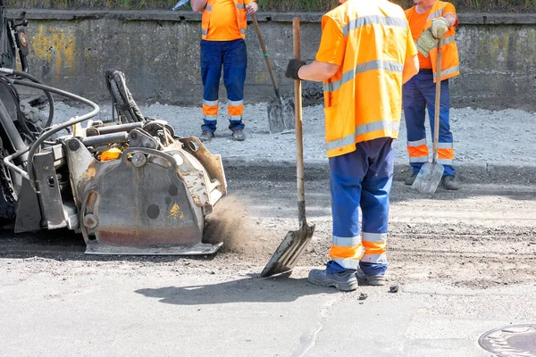 在一队身穿橙色工作服的道路工人的包围下 一个工业铣头正在工作 并正在清除旧的沥青路面 以便随后修理道路 复制空间 — 图库照片