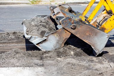 Güçlü metal bir buldozer kovası, eski yasfaltı yolun tamir edilmiş kısmından kazıyarak bir yığın haline getiriyor. Boşluğu kopyala.