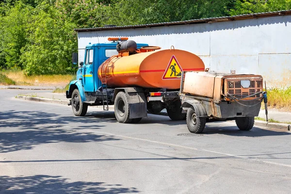 Güneşli bir günde hava basınçlı matkapla gezici bir inşaat kompresörünü taşıyan eski bir su tankeri kamyonu. Boşluğu kopyala.